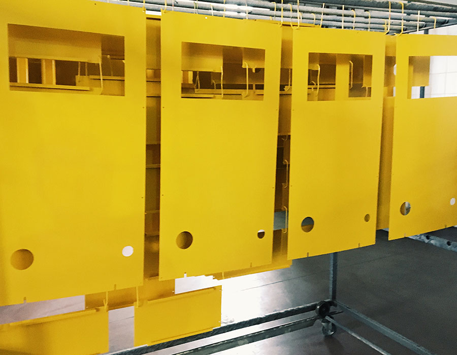 Yellow powder-coated metal panels hanging on a production line for industrial equipment manufacturing.