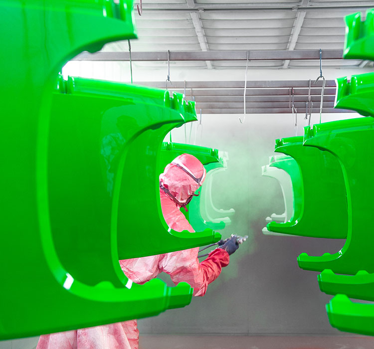 Technician applying green powder coating to metal equipment components in an industrial finishing facility.